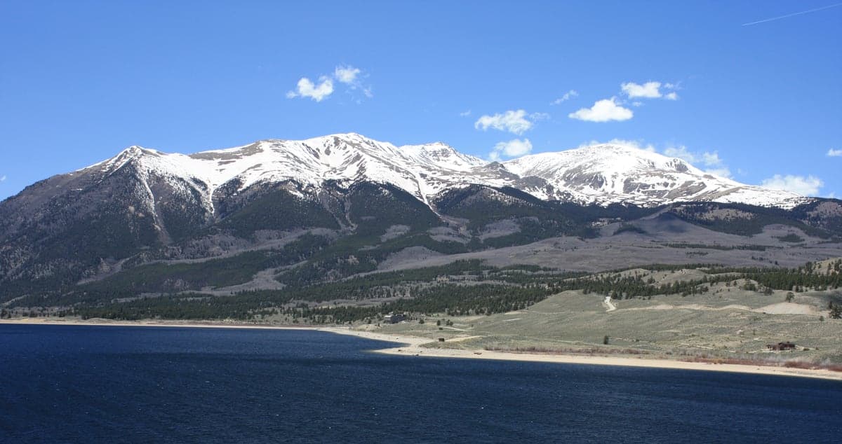 Mount Elbert rises beyond the blue water and wooded shore of Twin Lakes.