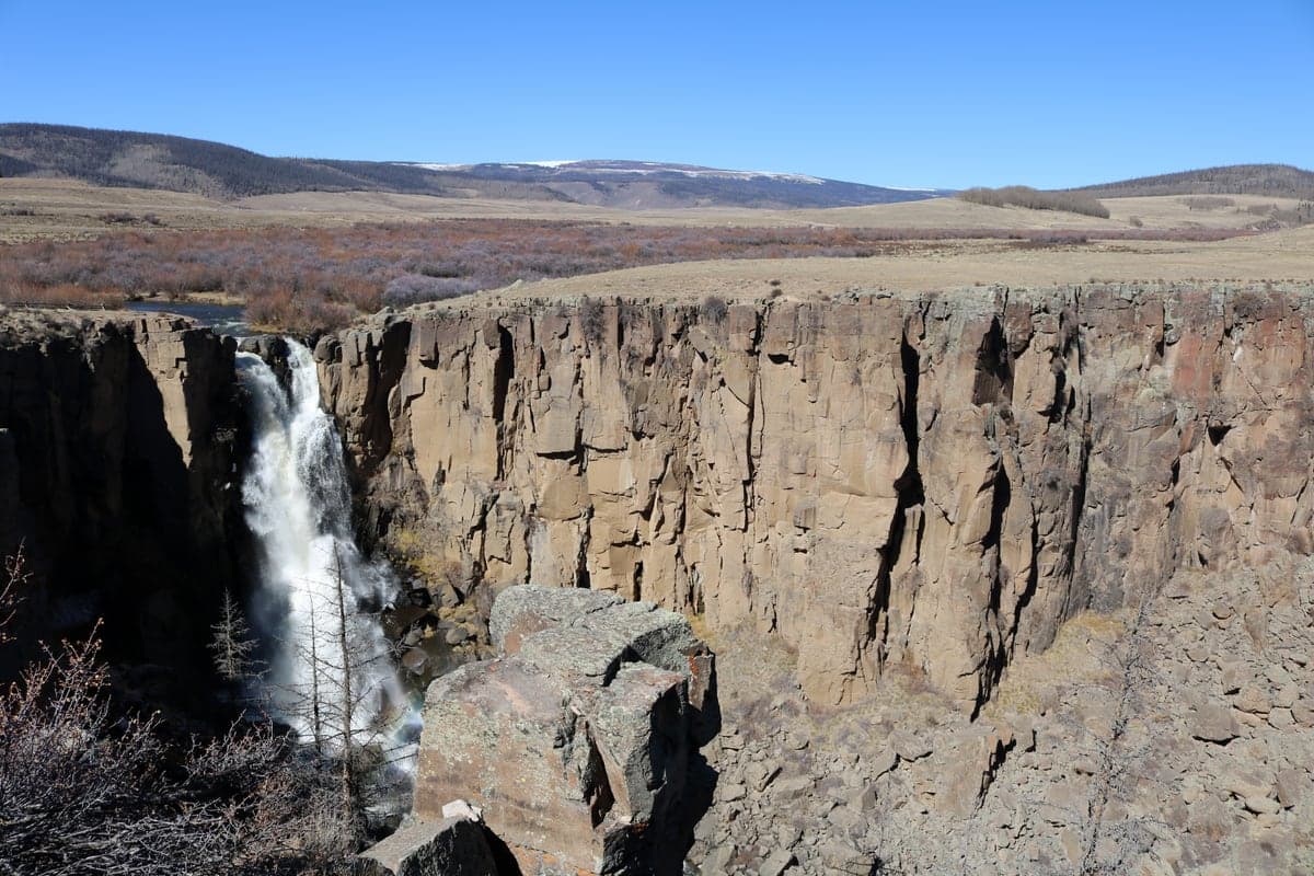 North Clear Creek Falls drops beside tall volcanic cliffs beneath an open high-country plateau.