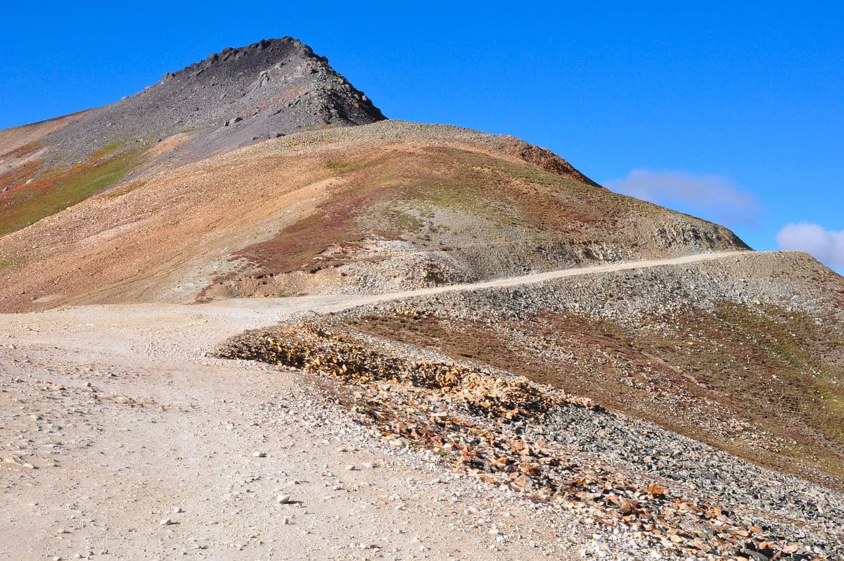 A pale gravel road traverses the rust-colored, above-treeline slopes of Engineer Mountain on the Alpine Loop.