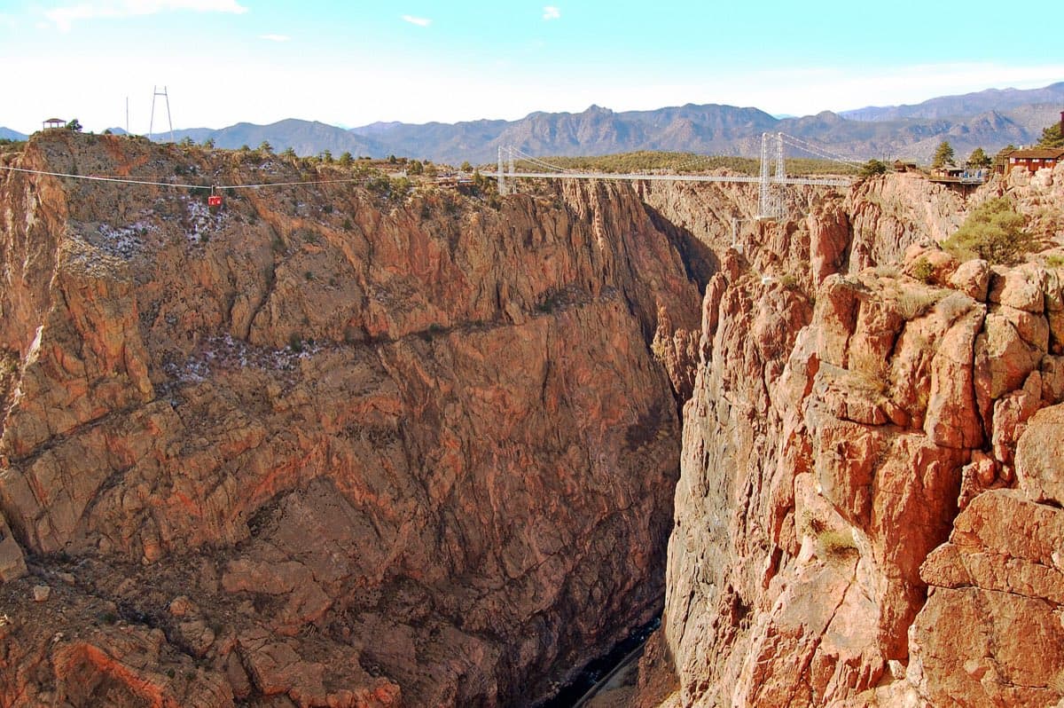 The Royal Gorge Bridge spans the sunlit, sheer-sided gorge west of Cañon City, with mountains beyond.
