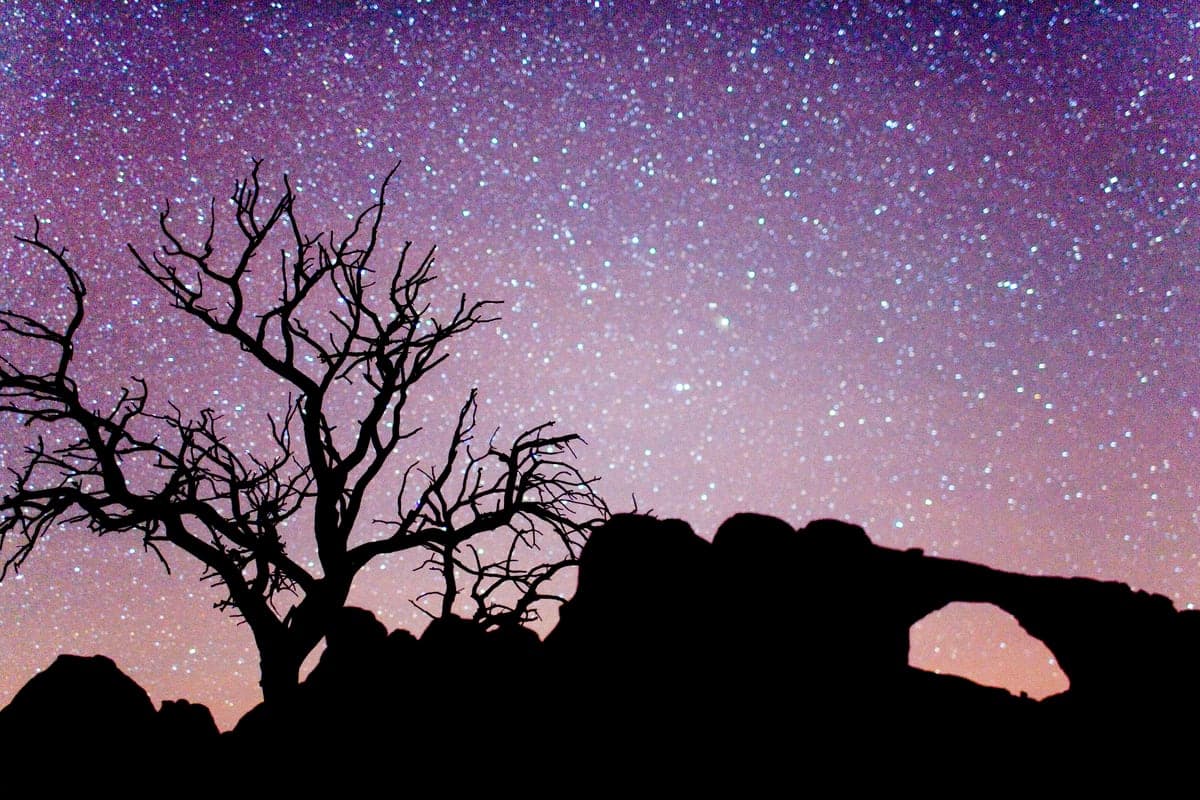 A star-filled night sky above a silhouetted sandstone arch in Arches National Park
