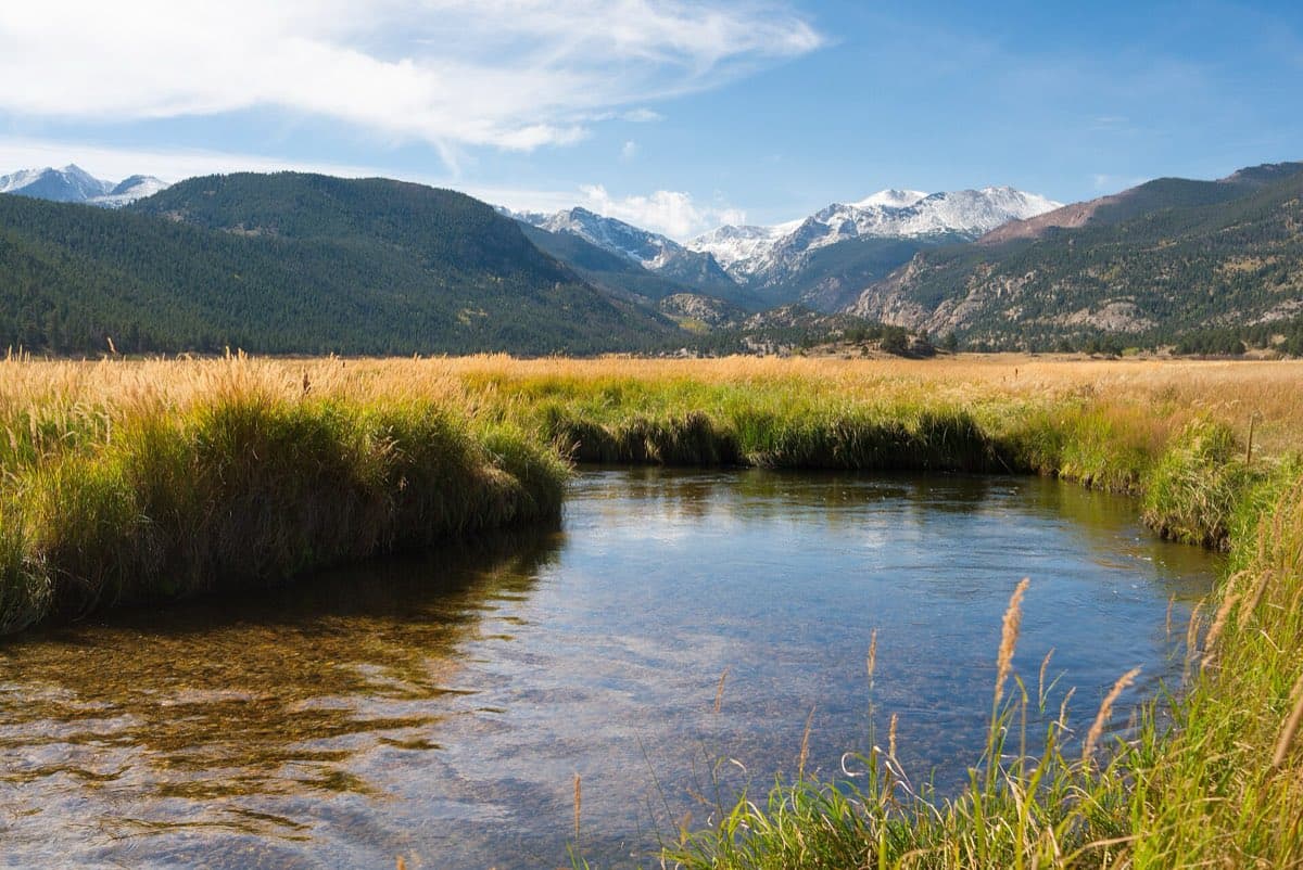 The Big Thompson River winding through Moraine Park beneath golden meadow grass and snow-dusted peaks.
