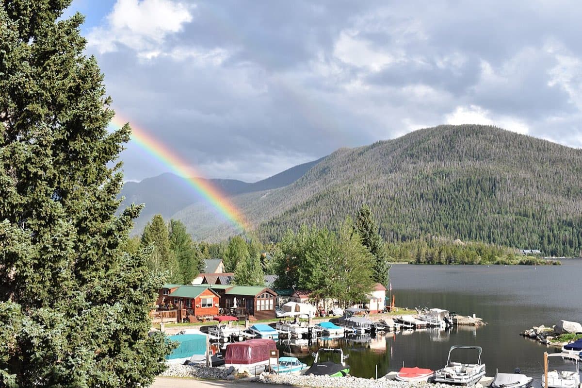 A vivid rainbow arcs above Grand Lake, a marina, and forested Colorado mountains.