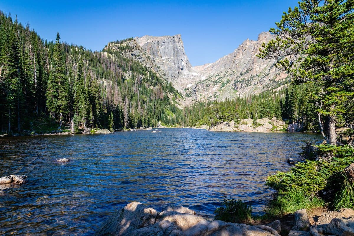 Dream Lake below Hallett Peak and the rocky Continental Divide, framed by evergreen forest on a clear summer morning.