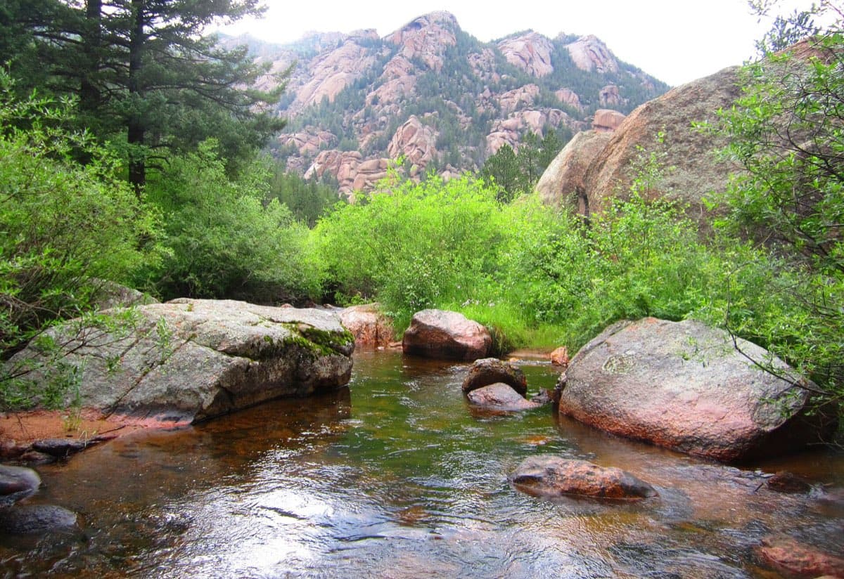 Goose Creek flowing around granite boulders beneath forested rock ridges in Lost Creek Wilderness.
