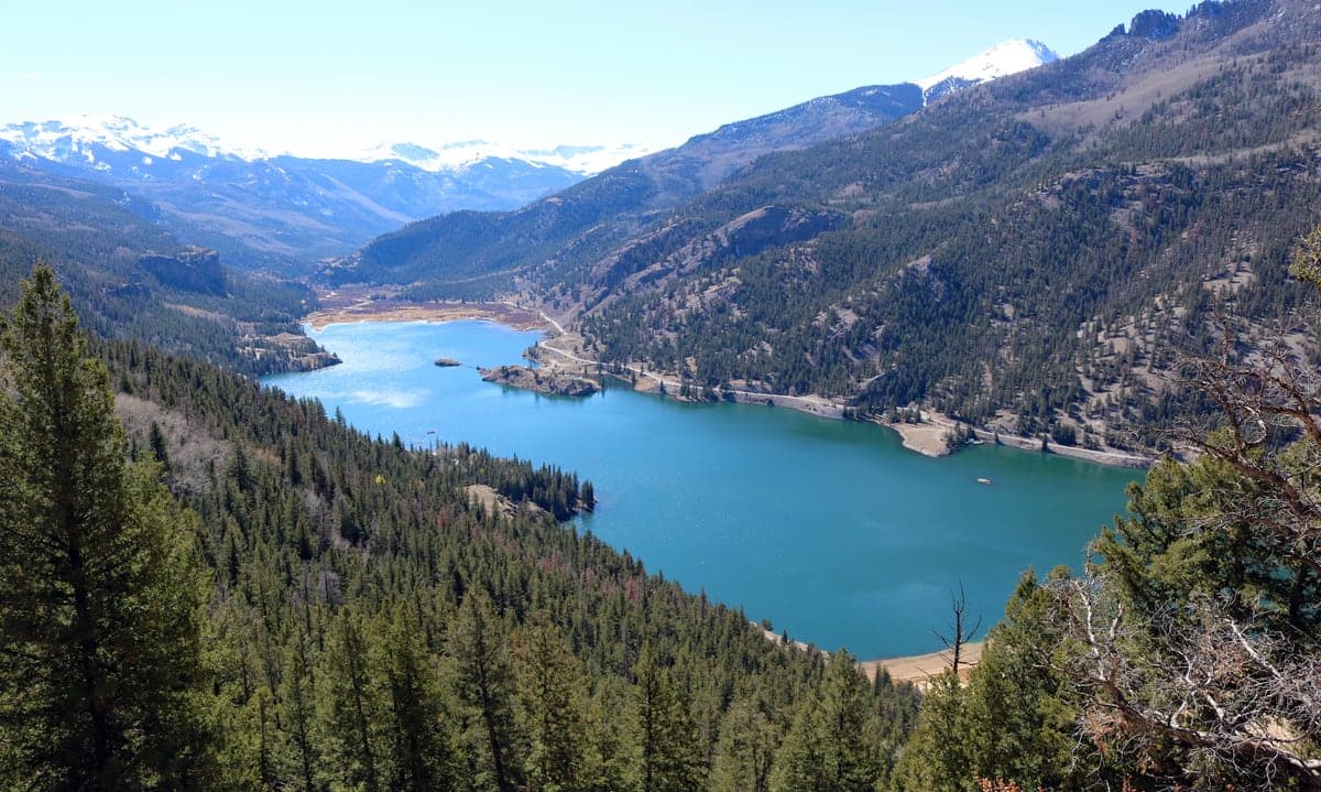 Lake San Cristobal curves through a forested San Juan Mountains valley below snow-streaked peaks.