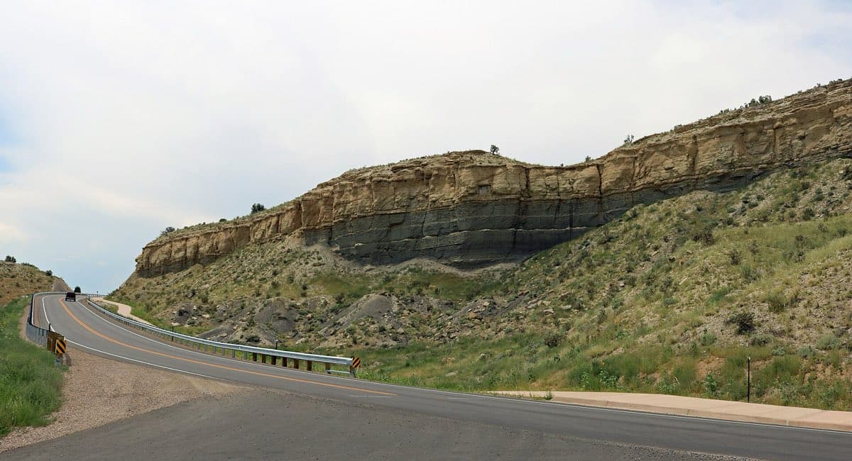 Layered sandstone and dark shale rise above Juniper Road in Lake Pueblo State Park.