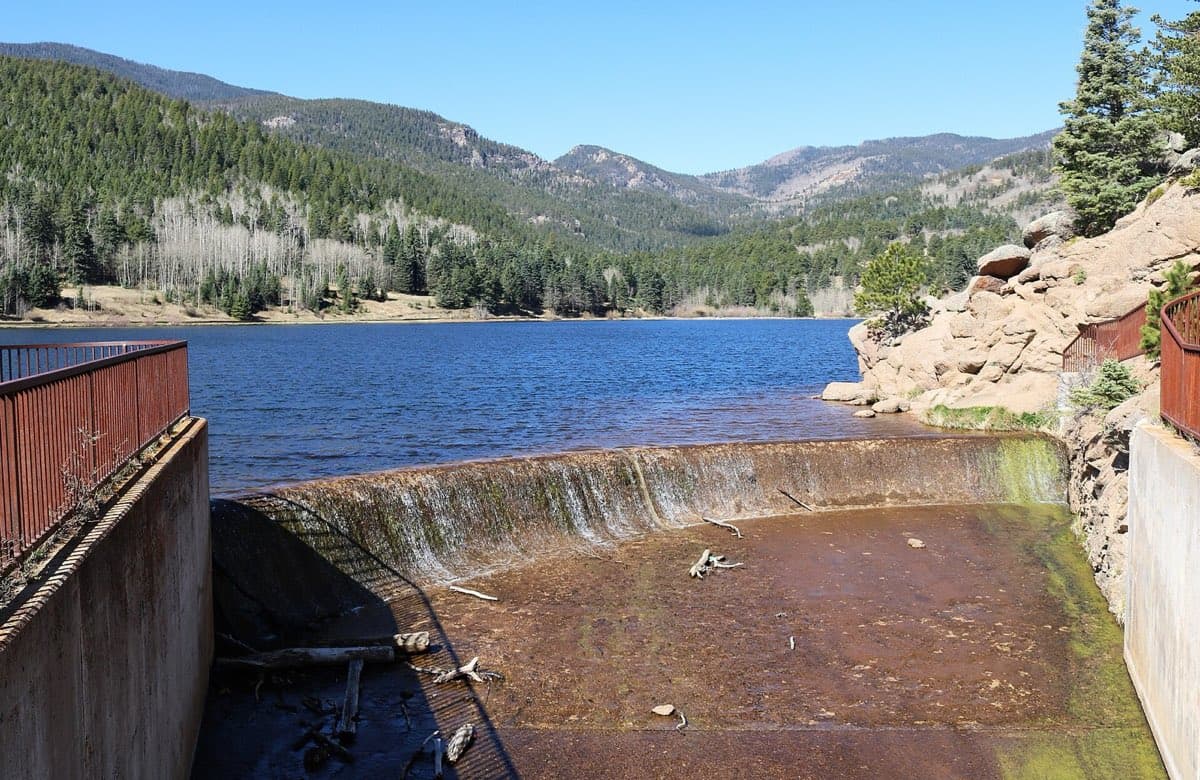 Lake Isabel stretches toward the wooded Wet Mountains under a clear sky.