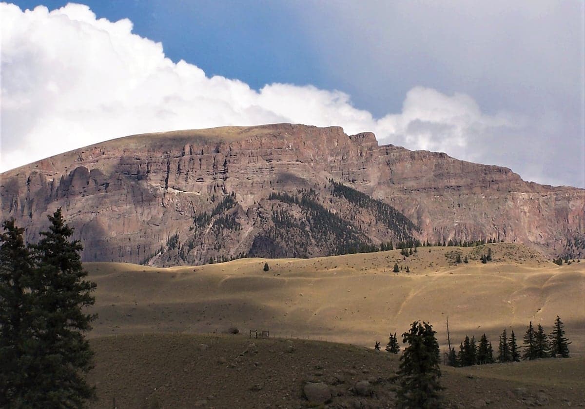 The broad volcanic cliffs of Bristol Head rise above open meadow and scattered spruce near Creede.