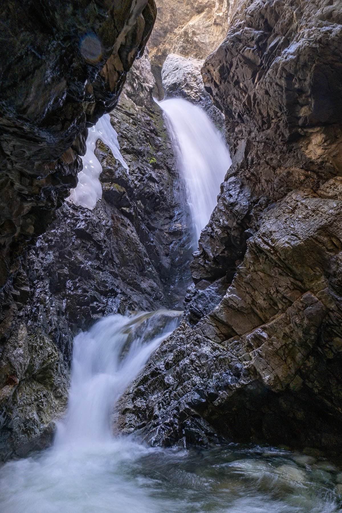 Zapata Falls pours through a narrow, dark rock cleft with lingering ice beside the cascade.