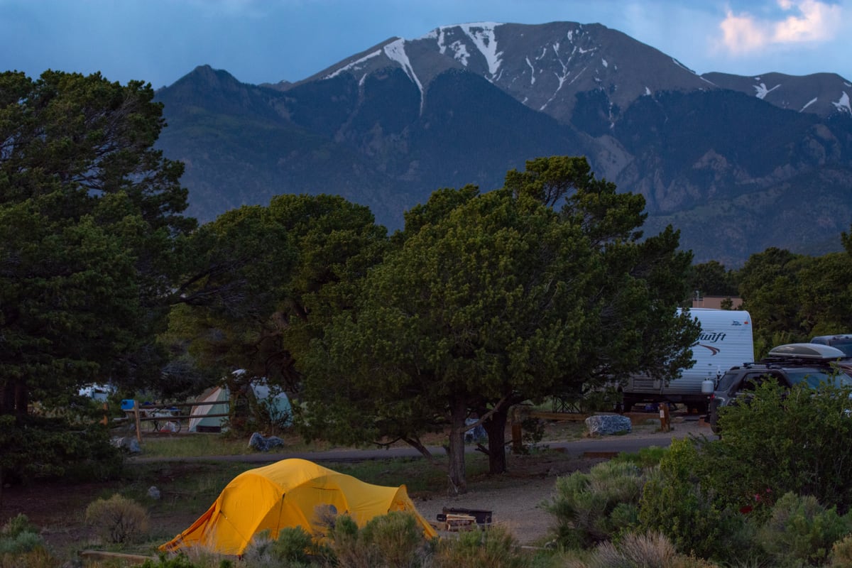 Tents and RVs among juniper trees at Piñon Flats Campground beneath the Sangre de Cristo Mountains