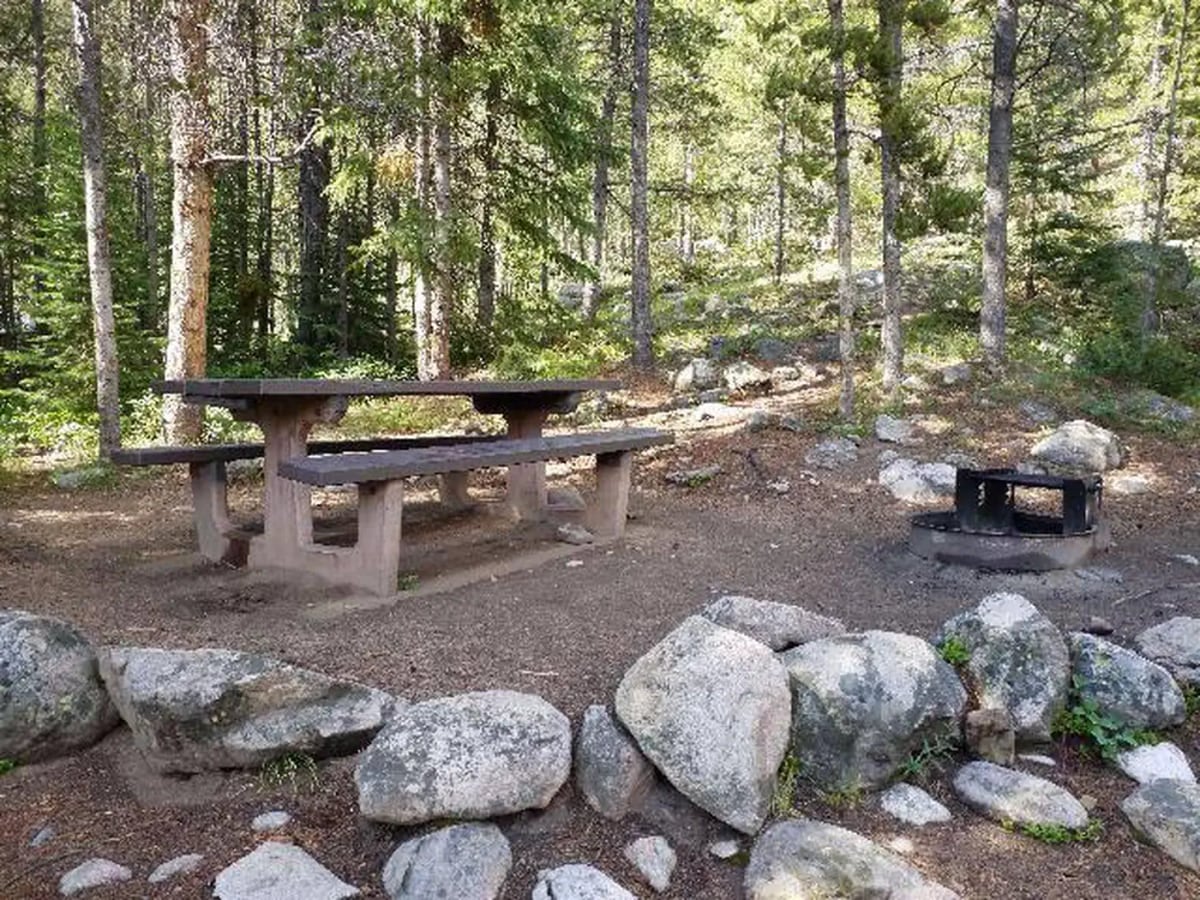 Stone picnic table and fire ring among pines and boulders at May Queen Campground