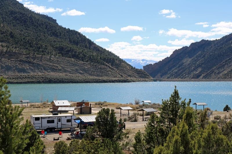Developed campsites and picnic shelters beside Rifle Gap Reservoir with mountains beyond