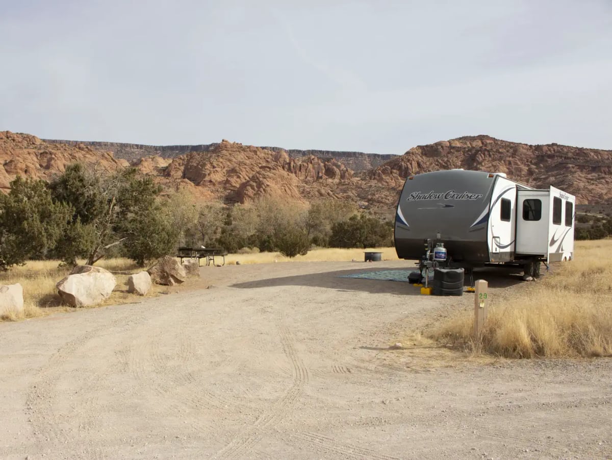 Travel trailer, picnic table, and fire ring in a campsite at Ken's Lake Campground below red-rock cliffs