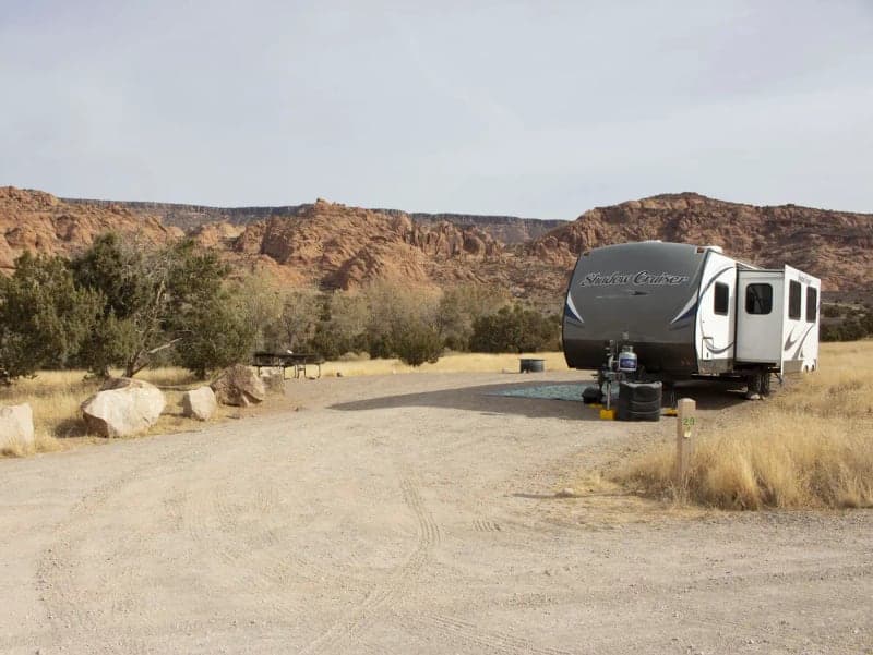 Travel trailer, picnic table, and fire ring in a campsite at Ken's Lake Campground below red-rock cliffs