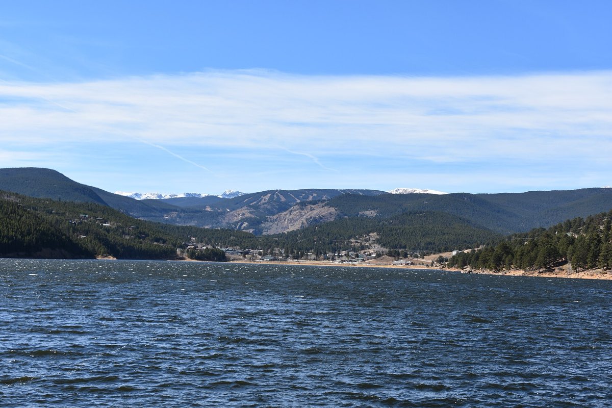 Barker Reservoir in the foreground, with Nederland homes, forested ridges, and snow-covered peaks beyond.