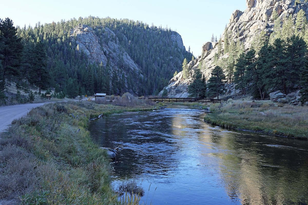 The South Platte River flowing past a footbridge between pine-covered granite walls at Eleven Mile Picnic Area.