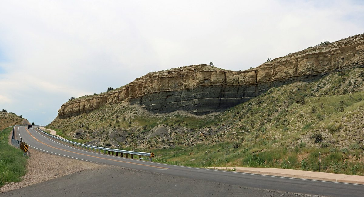 Layered sandstone and dark shale rise above Juniper Road in Lake Pueblo State Park.