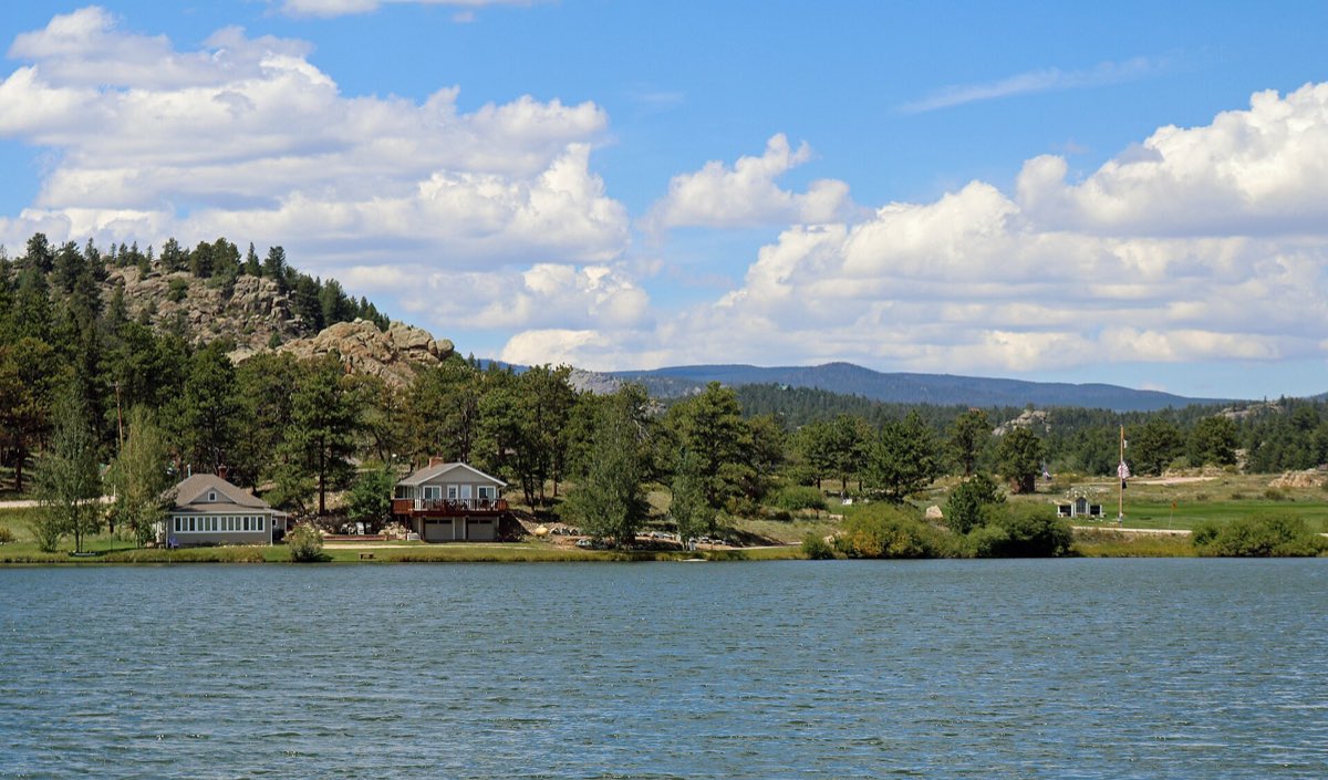 Ramona Lake bordered by homes, pine-covered outcrops, and open parkland in Red Feather Lakes.