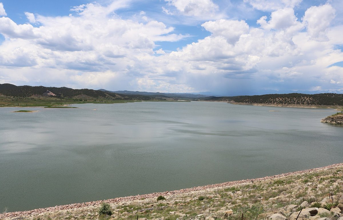 Trinidad Lake stretches west beneath summer clouds, with dry foothills around the shoreline.